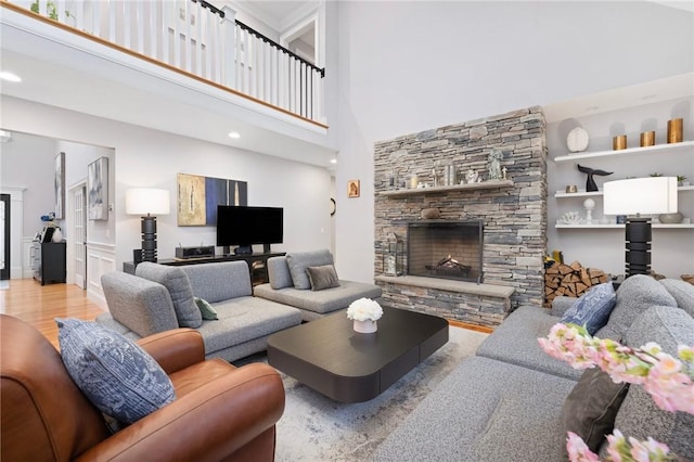 living room with a towering ceiling, light wood-type flooring, and a stone fireplace