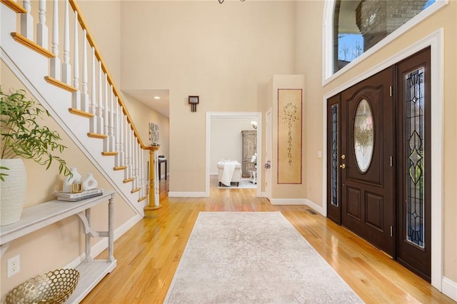 foyer with light wood-type flooring and a towering ceiling