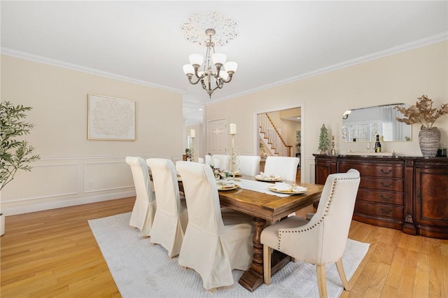 dining room featuring light wood-type flooring, ornamental molding, and an inviting chandelier