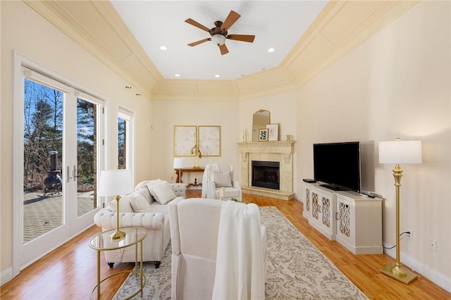 living room featuring ceiling fan, light wood-type flooring, ornamental molding, and a tile fireplace