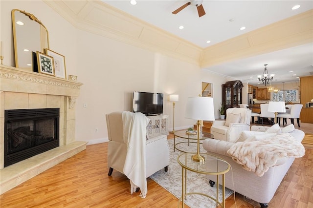 living room featuring ceiling fan with notable chandelier, crown molding, a tile fireplace, and light hardwood / wood-style flooring