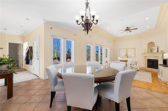 tiled dining room featuring a tile fireplace, ceiling fan with notable chandelier, crown molding, and a healthy amount of sunlight