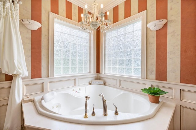 bathroom with a tub to relax in, a wealth of natural light, an inviting chandelier, and ornamental molding