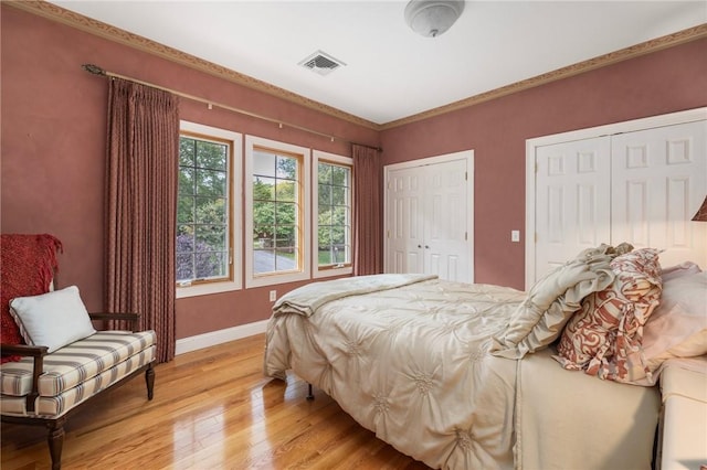 bedroom with two closets, light hardwood / wood-style flooring, and crown molding