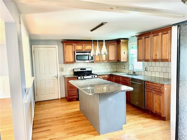 kitchen with light stone countertops, sink, hanging light fixtures, stainless steel appliances, and a kitchen island