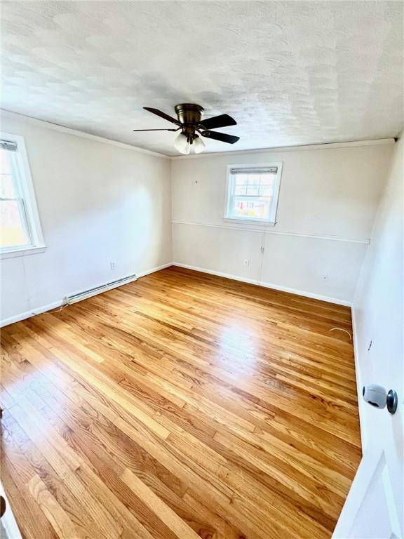 empty room with ceiling fan, light hardwood / wood-style floors, a textured ceiling, and a baseboard radiator