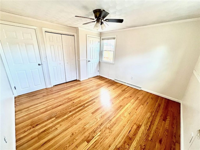 unfurnished bedroom with crown molding, ceiling fan, light wood-type flooring, a baseboard radiator, and multiple closets