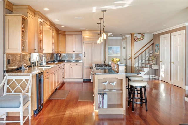 kitchen featuring sink, light brown cabinetry, decorative light fixtures, dark hardwood / wood-style flooring, and a breakfast bar area