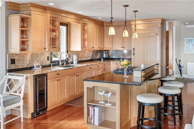 kitchen featuring light brown cabinetry, hardwood / wood-style flooring, hanging light fixtures, and sink