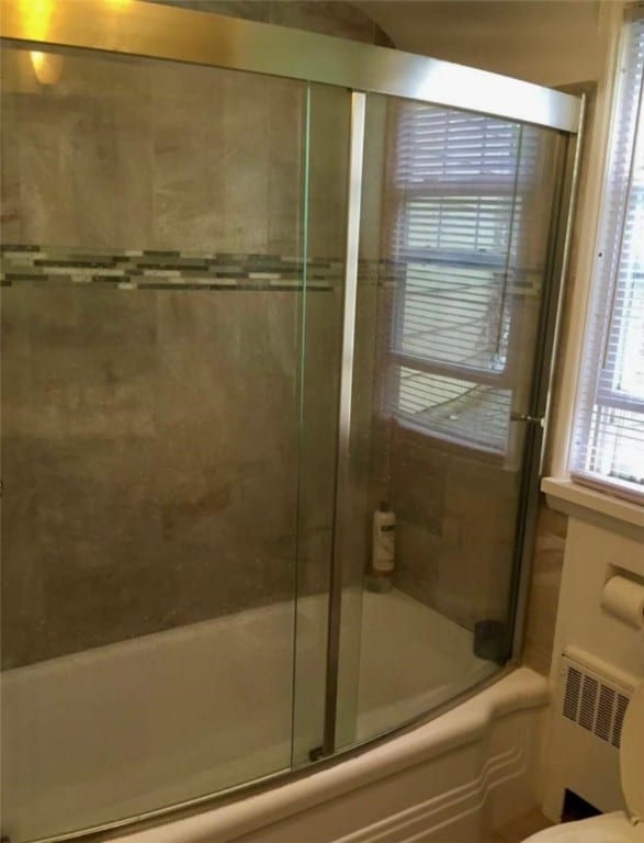 bathroom with radiator, enclosed tub / shower combo, and toilet