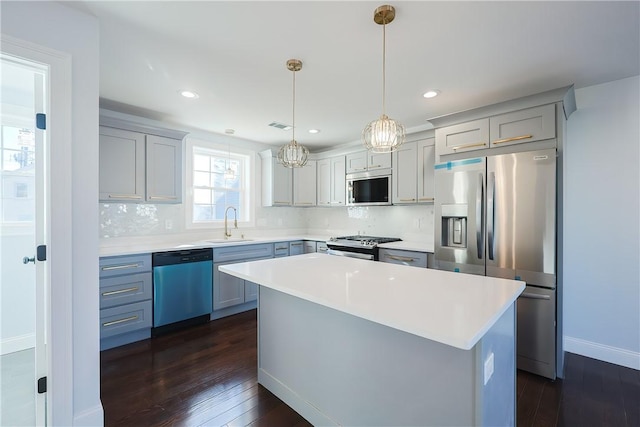 kitchen with appliances with stainless steel finishes, backsplash, dark wood-type flooring, a center island, and hanging light fixtures