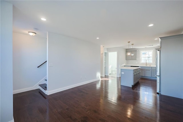 kitchen featuring stainless steel fridge, dark wood-type flooring, sink, decorative light fixtures, and a kitchen island