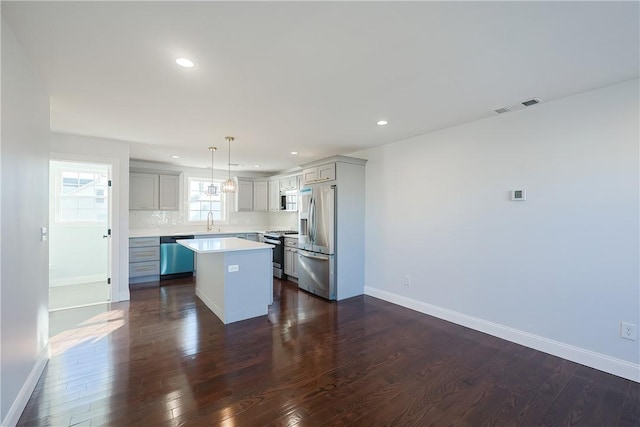 kitchen with appliances with stainless steel finishes, dark wood-type flooring, sink, a center island, and hanging light fixtures