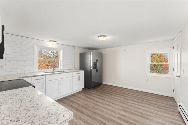 kitchen with plenty of natural light, stainless steel fridge, white cabinetry, and baseboard heating