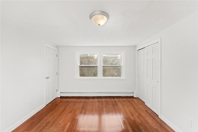 unfurnished bedroom with a closet, a baseboard radiator, and wood-type flooring