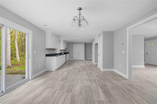 unfurnished living room with sink, a notable chandelier, and light wood-type flooring