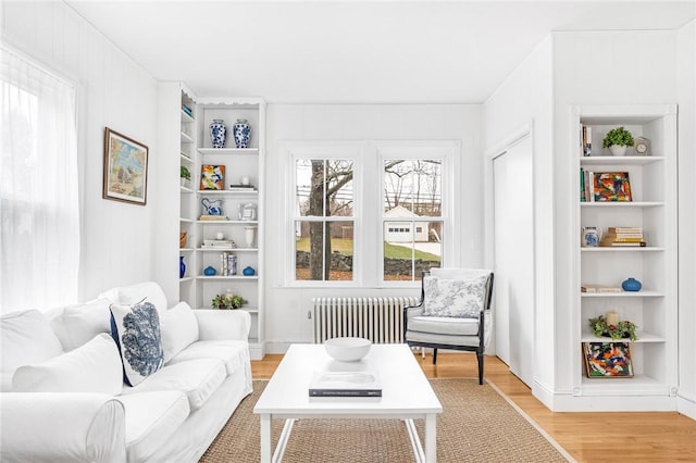 living area with built in shelves, hardwood / wood-style flooring, and radiator