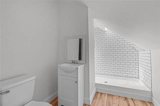 bathroom featuring tiled shower, wood-type flooring, vanity, and toilet