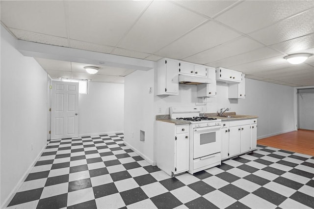 kitchen with white gas range, white cabinetry, a drop ceiling, and sink