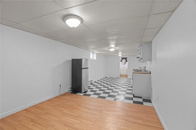 basement with a drop ceiling, stainless steel fridge, and light hardwood / wood-style flooring