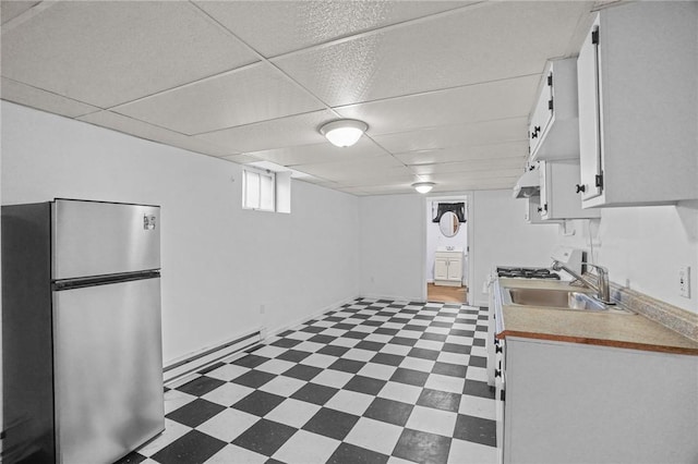 basement featuring a paneled ceiling, sink, stainless steel refrigerator, and a baseboard heating unit