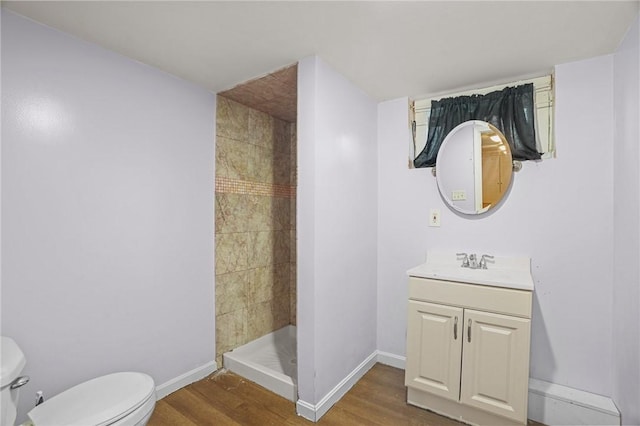 bathroom featuring tiled shower, vanity, wood-type flooring, and toilet