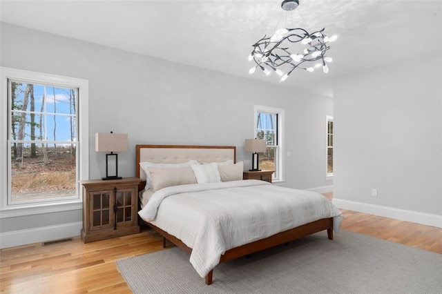 bedroom featuring multiple windows, an inviting chandelier, and light wood-type flooring