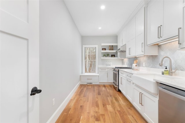 kitchen featuring sink, appliances with stainless steel finishes, tasteful backsplash, light hardwood / wood-style floors, and white cabinetry