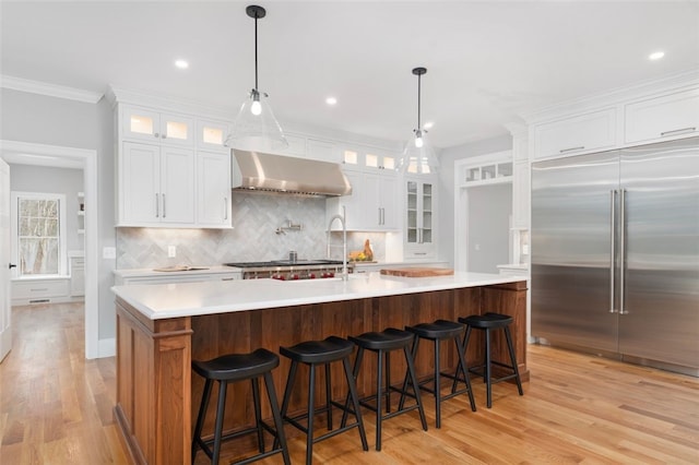 kitchen featuring a center island with sink, wall chimney range hood, light hardwood / wood-style floors, white cabinetry, and stainless steel appliances