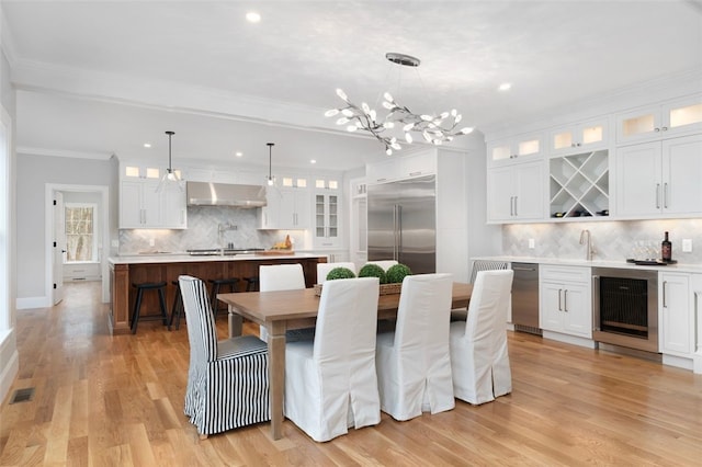 dining room with sink, crown molding, light wood-type flooring, a notable chandelier, and beverage cooler