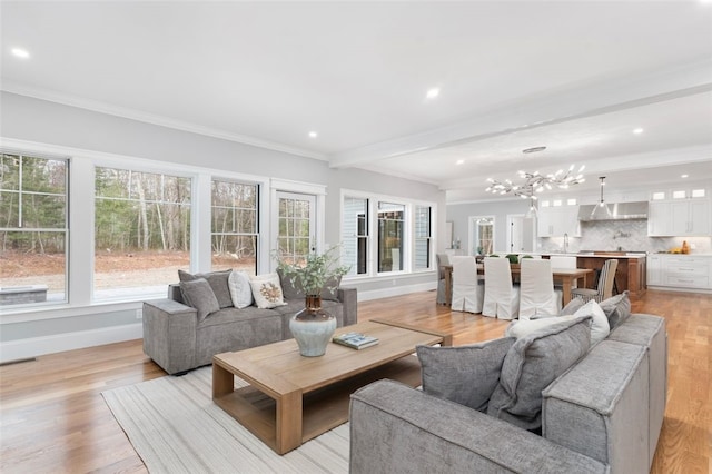 living room with a notable chandelier, beam ceiling, light wood-type flooring, and ornamental molding