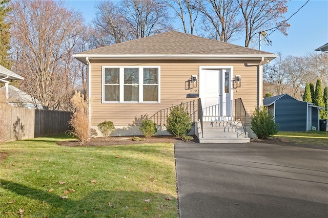 bungalow-style home featuring roof with shingles, fence, and a front yard