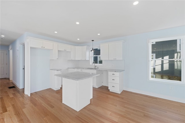 kitchen featuring recessed lighting, light wood-style floors, white cabinetry, a kitchen island, and a sink