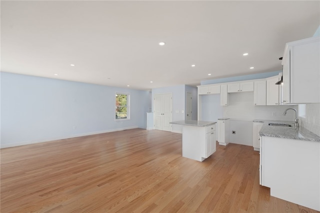 kitchen featuring a sink, white cabinetry, light wood-type flooring, decorative backsplash, and light stone countertops