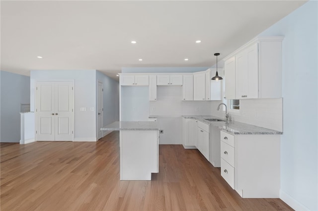 kitchen with light wood-style flooring, a sink, a kitchen island, white cabinetry, and tasteful backsplash