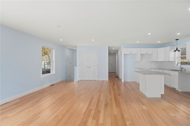 kitchen with light wood-style floors, a kitchen island, white cabinets, and a sink