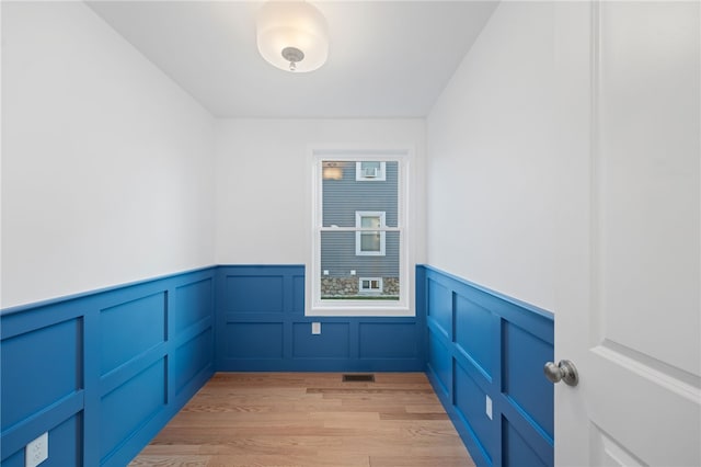 spare room featuring light wood-type flooring, visible vents, and wainscoting