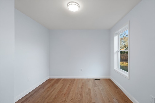 empty room with light wood finished floors, visible vents, and baseboards