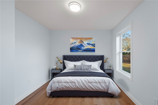 bedroom with multiple windows, wood finished floors, and baseboards