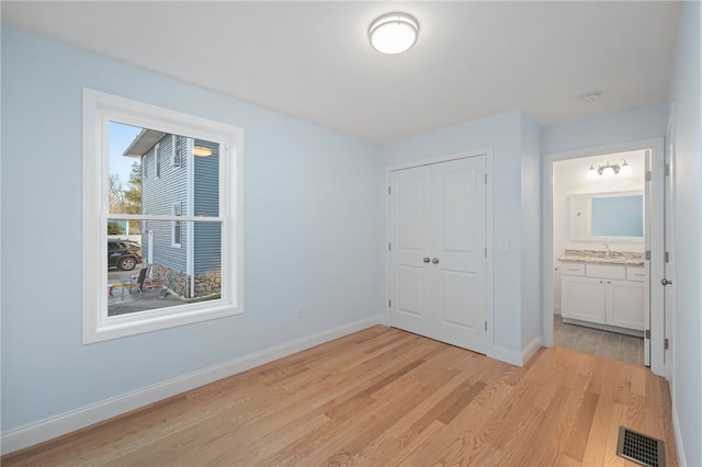 unfurnished bedroom featuring light wood finished floors, baseboards, visible vents, and a closet