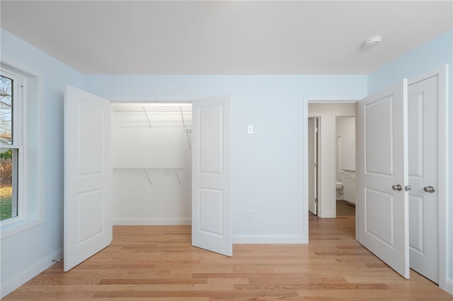 unfurnished bedroom with multiple windows, a closet, light wood-style flooring, and baseboards