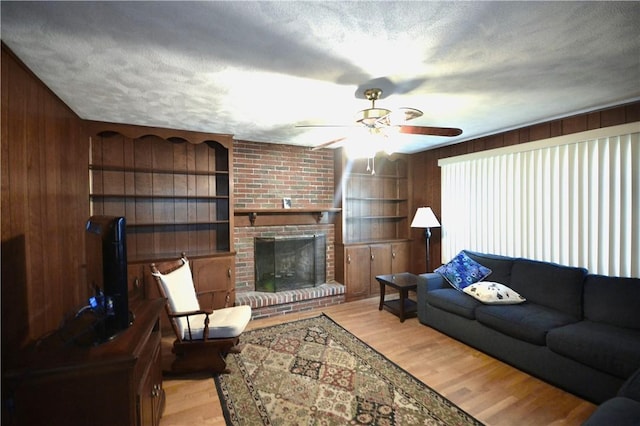 living room with a brick fireplace, light hardwood / wood-style flooring, wooden walls, and a textured ceiling