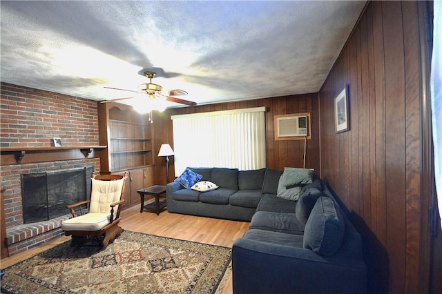 living room with wooden walls, light wood-type flooring, a fireplace, and a wall unit AC