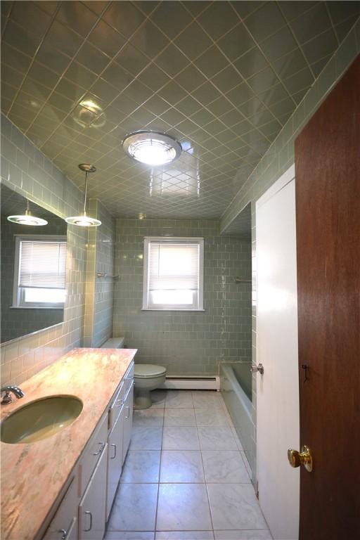 full bathroom featuring vanity, a baseboard heating unit, tile patterned flooring, toilet, and tile walls