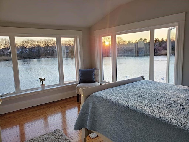 bedroom with hardwood / wood-style flooring, a water view, access to exterior, and vaulted ceiling