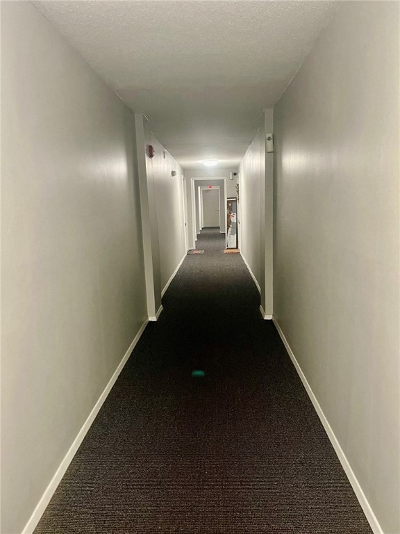 hallway with a textured ceiling and dark carpet