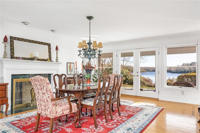 dining area with an inviting chandelier, french doors, a water view, hardwood / wood-style flooring, and a fireplace