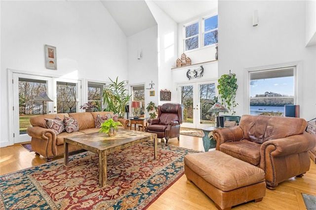 living room featuring a water view, light wood-type flooring, high vaulted ceiling, and french doors