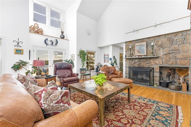 living room with wood-type flooring, a fireplace, high vaulted ceiling, and french doors