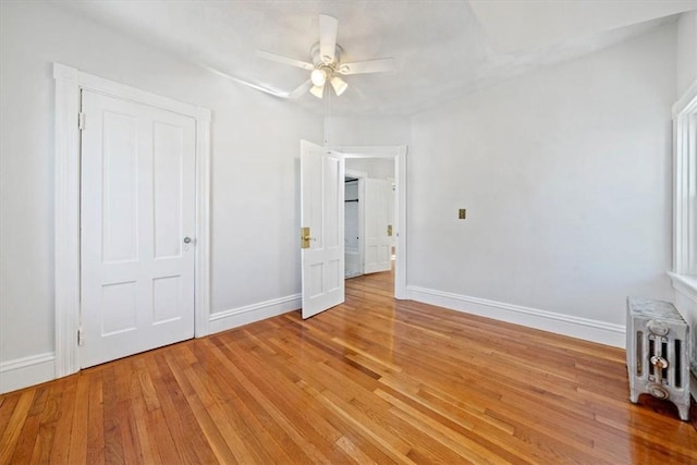 unfurnished bedroom with a closet, ceiling fan, radiator heating unit, and hardwood / wood-style flooring